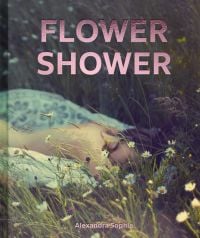 Low angled shot of daisies in prairie landscape with blurred image of nude female laying on front with FLOWER SHOWER in pink metallic font above