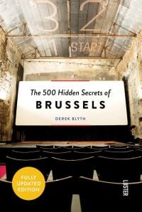 Colour photo of a view from a cinema seat in a derelict theatre, looking at a white screen with The 500 Hidden Secrets of Brussels in black font