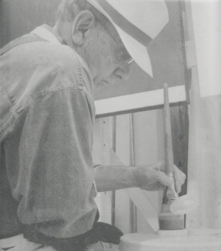 Sepia profile photo of artist James Howell in white hat painting with left hand