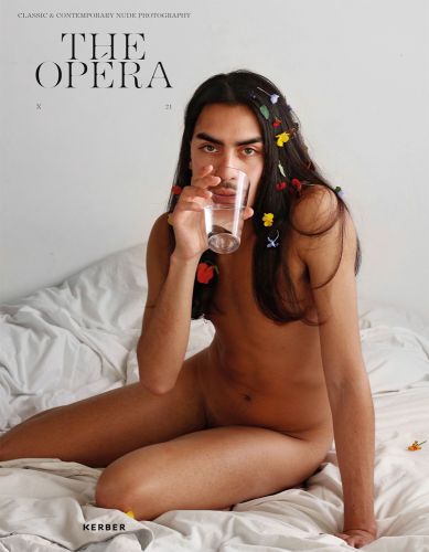 Nude male model with long black hair in seated pose on white bed sheets drinking glass of water and The Opéra in black font to top right