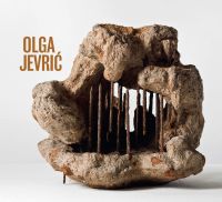 Photograph of industrial rock sculpture with rusted metal poles, in white exhibition space, 'OLGA JEVRI?', in orange font to upper left, by Ridinghouse.