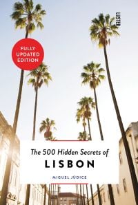 Row of towering palm trees down sunny street, The 500 Hidden Secrets of Lisbon in black font on white banner below