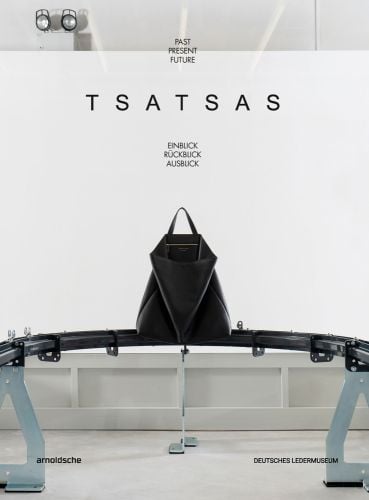 Large black leather bag on metal metal conveyer belt, on white cover, 'TSATSAS, past present future', by Arnoldsche Art Publishers.