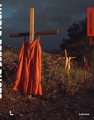 Orange and cream dresses hanging from 3 wooden crosses in ground, World Press Photo in cut-out font with orange surround, 2022 in orange font