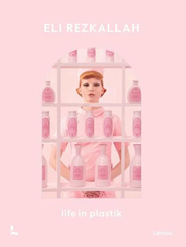 Model in pink tunic and hat, standing behind shelves of pink plastic product bottles, on pink cover, 'Eli Rezkallah, Life in Plastik' by Lannoo Publishers.