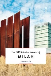 Tall rusted metal panelled structure surrounded by pale dry grass, tall building behind, The 500 Hidden Secrets of MILAN in black font on bottom white banner.