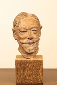 Sculpture of male head with large moustache, mounted on wood plinth.
