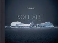 Two large icebergs floating on water in Antarctica, TOM NAGY, SOLITAIRE, in white font above.