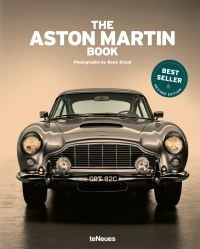 Front end of silver Aston Martin DB5, headlights on, THE ASTON MARTIN BOOK, in white font above, 'BEST SELLER' in white font to green circle.