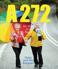 Book cover of A272-An Ode to a Road, with Pieter and Rita Boogaart walking hand-in-hand down the A272, Rita holding a large rainbow umbrella. Published by Pallas Athene.