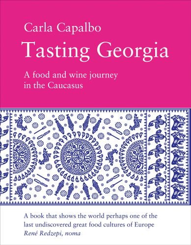 Traditional Georgian cotton tablecloth painted in various hues of blue, 'Tasting Georgia: A Food and Wine Journey in the Caucasus', in white font to pink banner above.
