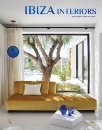Interior living space with mustard velvet chaise longue, view outside with tree and swimming pool, on cover of 'Ibiza Interiors', by Lannoo Publishers.