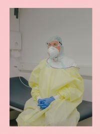 Person in yellow medical gown, blue gloves face mask and goggles, sitting on hospital bed, on cover of 'Ingmar Björn Nolting, About the Days Ahead', by Verlag Kettler.