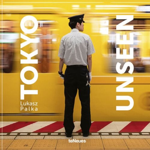 Japanese subway staff member standing next to speeding yellow train, on cover of 'Tokyo Unseen', by teNeues Books.