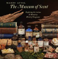 Collection of antique perfume bottles surrounded by old books and chunks of wood, on cover of 'The Museum of Scent, Exploring the Curious and Wondrous World of Fragrance', by Abbeville Press.