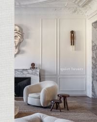 Cool white interior with panelled walls, tub chair, marble fireplace, on cover of 'Quiet Luxury', by Beta-Plus.