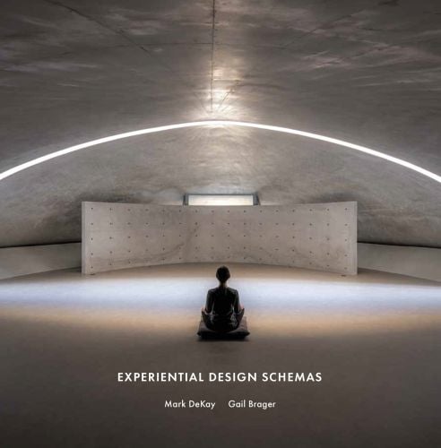 Person sitting cross-legged on cushion, in domed building space with strip of light above, on cover of 'Experiential Design Schemas', by ORO Editions.