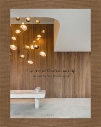 Book cover of The Art of Craftsmanship, Interiors by Van Overstraeten, with interior with wood paneled wall, low hanging modern light fitting, and marble seat. Published by Beta-Plus.