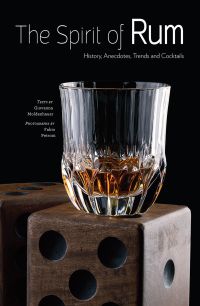 Crystal glass of rum on wooden dice box, on cover of 'The Spirit of Rum, History, Anecdotes, Trends and Cocktails', by White Star.