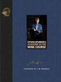 Man wearing blue jacket, standing in wine cellar, holding a bottle wine, on blue cover of 'Steven Spurrier's Académie du Vin Wine Course, The Art of Learning by Tasting', by Academie du Vin Library.