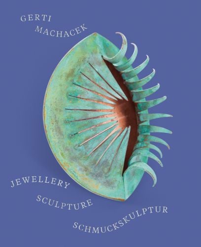 Blue book cover of Gerti Machacek, Jewellery Sculpture, featuring an oxidised copper jewellery piece, shaped like an eye, with eyelashes. Published by Arnoldsche Art Publishers.