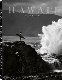 Book cover of Olaf Heine's Hawaii, with surfer standing on rocks holding surf board near the crashing waves of the sea. Published by teNeues Books.