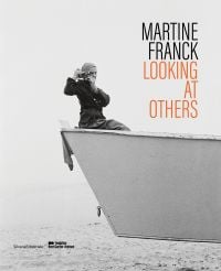 Book cover of Martine Franck: Looking at Others, with the photographer sitting in a skip while taking a photograph of the viewer. Published by Silvana.