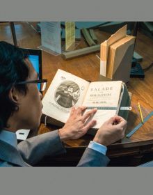 Group of people looking through large library books, on grey cover, Photographing Shakespeare in gold font below