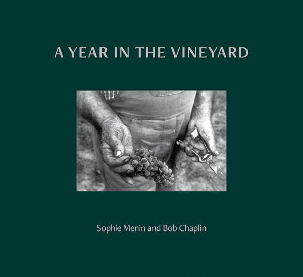 Book cover of A Year in the Vineyard with worker holding secateurs and a bunch of grapes. Published by Cultureshock.