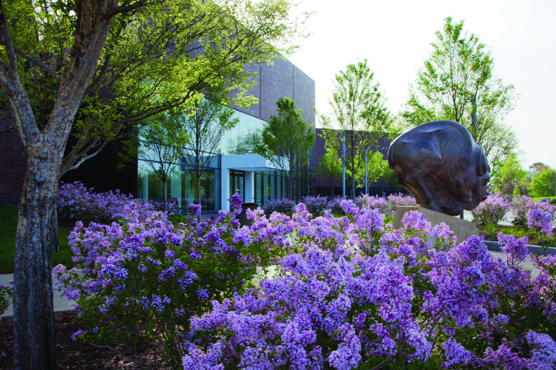 Large jagged edge sculpture on grey plinth in garden with trees, The Art Garden Wichita Art Museum in white font above