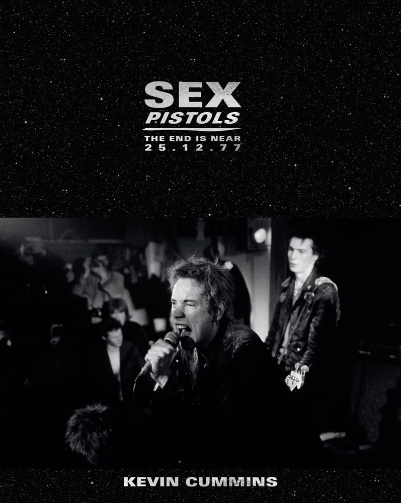 Black and white photograph of Johnny Rotten and Sid Vicious on stage with an audience in the background and Sex Pistols The End is Near 25 12 77 Kevin Cummins in white