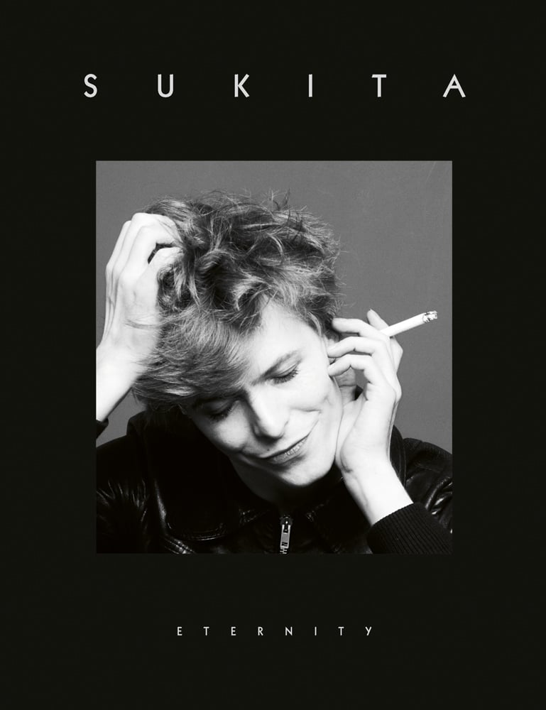 A black and white photo of David Bowie, head tilted down, wry grin and cigarette in hand with title Sukita above and Eternity below.