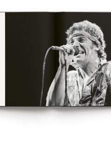 Bruce Springsteen wearing bandana, playing electric guitar on stage, on cover of 'Bruce Springsteen Live in the Heartland Photos by Janet Macoska', by ACC Art Books.