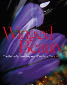 Purple wing shape above blurred blue and yellow gemstones, on cover of 'Winged Beauty, The Butterfly Jewellery Art of Wallace Chan', by ACC Art Books.