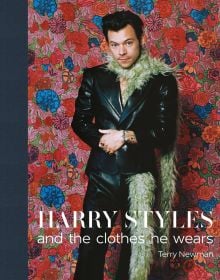 Harry Styles in black leather look suit, beige fur boa, floral backdrop, Harry Styles and the clothes he wears, in white font below, left navy border.
