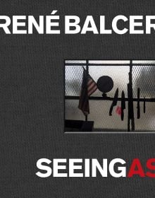 Row of knives and a machete, on magnetic strip, American flag and globe to left, on black cover of 'Seeing As, René Balcer', by ACC Art Books.