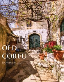 Book cover of Old Corfu, with a sunny village walkway leading to dark double doors of building, potted plants to right. Published by ACC Art Books.