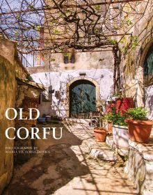 Sunny old village walkway to dark double doors of building, potted plants to right, on cover of 'Old Corfu' by ACC Art Books.