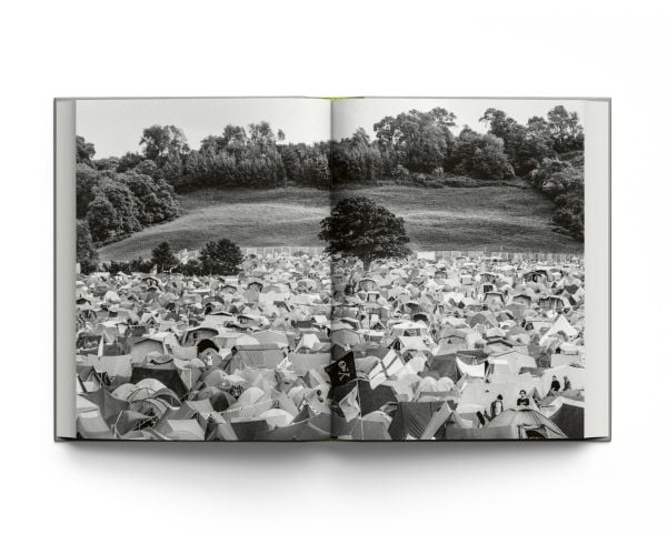 Book cover Liam Bailey's Glastonbury: The Festival and Its People, with festival goers standing at top of hill with tents behind them. Published by ACC Art Books.