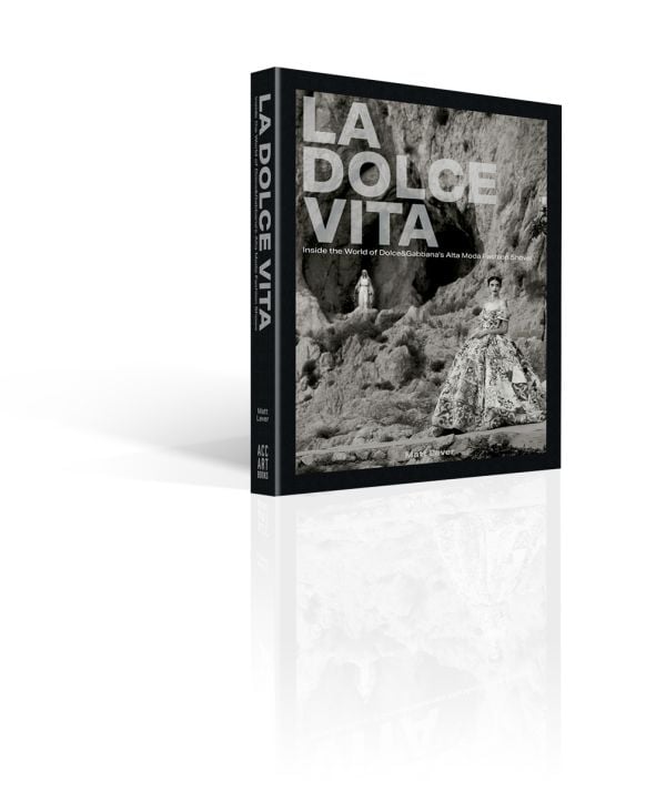 Book cover of La Dolce Vita: Inside the World of Dolce&Gabbana’s Alta Moda Fashion Shows, featuring a model in a large floral dress standing amongst a rocky mountain. Published by ACC Art Books.