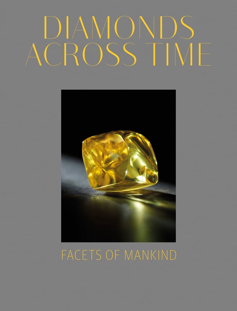 Yellow diamond on dark surface, glistening in light, on grey cover, DIAMONDS ACROSS TIME FACETS OF MANKIND in yellow font above and below.