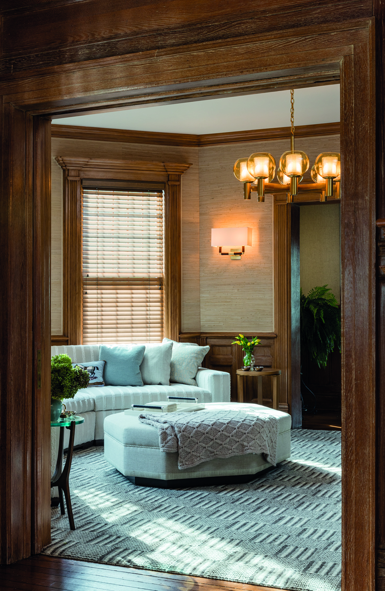 Beige interior space, central sofa, lit open fire, hanging light fittings, PENNY DRUE BAIRD On Interior Design in brown font above