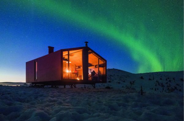 Book cover of Cabins: Escape to Nature, with modern cabin in a forest, with interior lights on. Published by Images Publishing.