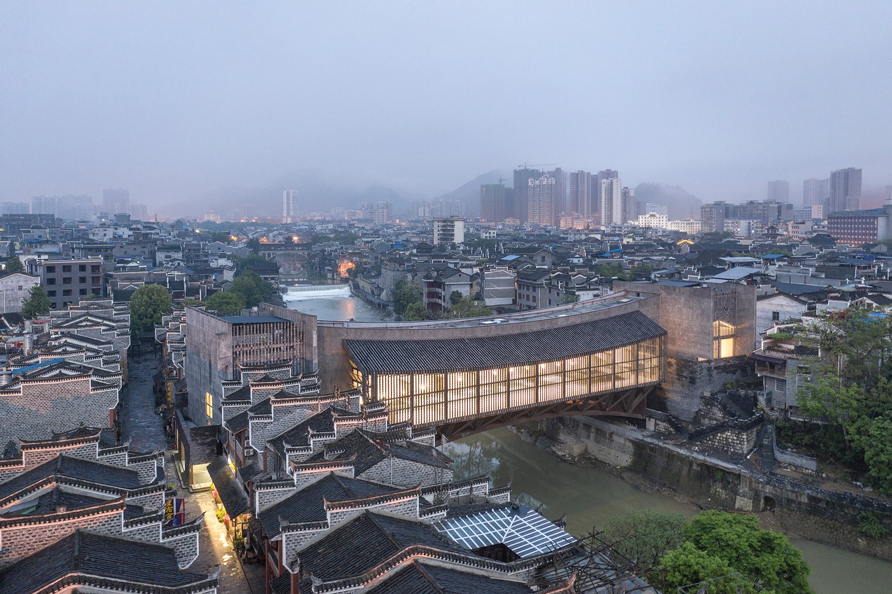 Building façade with dark grey modern exterior cover, ARCHITECTURE CHINA RE/DEFINE TRADITION in beige and white font above and below.