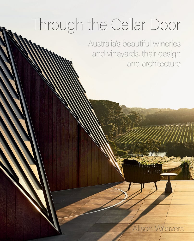 Outdoor view of modern architectural winery with vineyards in the distance and Through the Cellar Door in fine black font above