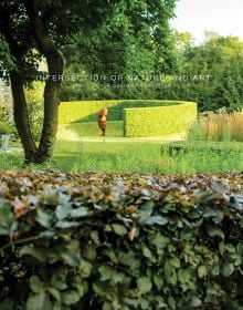 Landscaped garden with topiary hedge and sculpture of face, INTERSECTION OF NATURE AND ART, in small white font above centre cover.