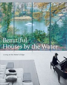 Book cover of Beautiful Houses by the Water: Living at the Water's Edge, featuring a pianist playing piano in living room interior with large windows, overlooking pond with fountain. Published by Images Publishing.