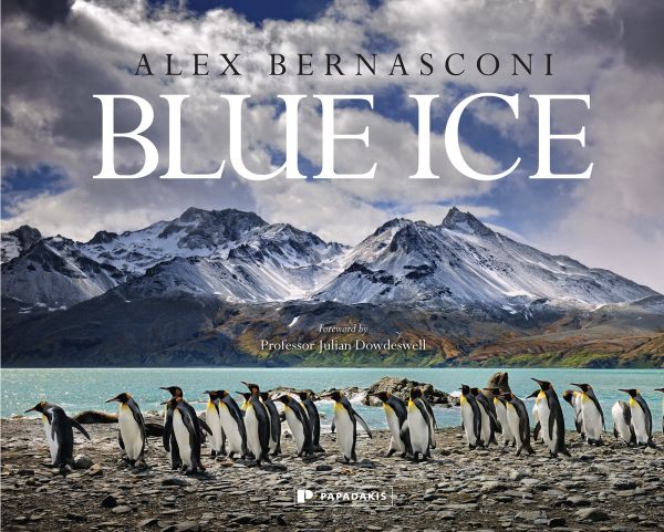 Book cover of Blue Ice, with snow covered mountains and a line of penguins below. Published by Papadakis.