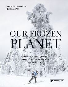 Book cover of Our Frozen Planet: A Photographic Journey Through the World of Snow and Ice, with a skier walking through a snow covered landscape. Published by Papadakis.