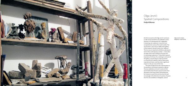 Photograph of industrial rock sculpture with rusted metal poles, in white exhibition space, 'OLGA JEVRI?', in orange font to upper left, by Ridinghouse.